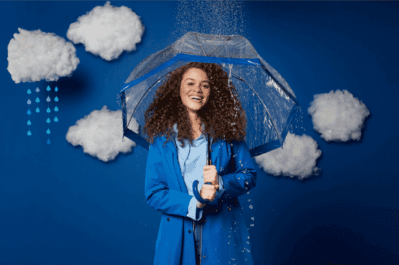 Woman with curly hair holding up umbrella to stop hair becoming frizzy from the atmosphere.