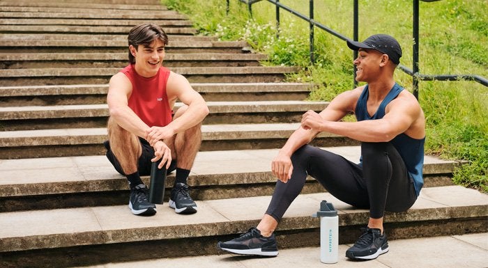 two men sitting on steps outside drinking protein shakes
