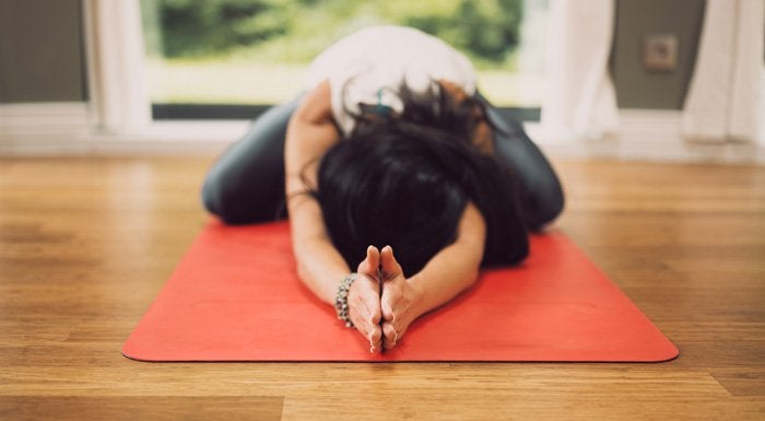 A woman doing a yoga stretch on a red yoga mat on the floor.