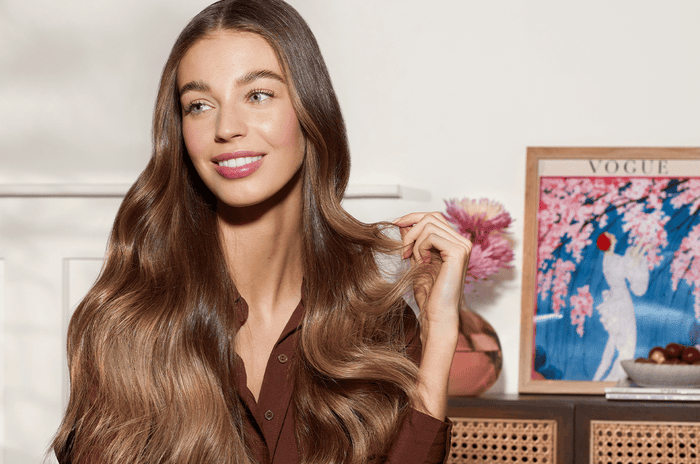 Woman smiling with long, beautiful brown hair. Behind her is a vintage Vogue cover in a frame.