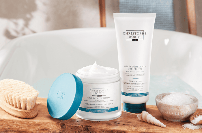 Two salon hair care products by Christophe Robin's Detox Regimen. White bottles with blue accents with sea salt next to them.