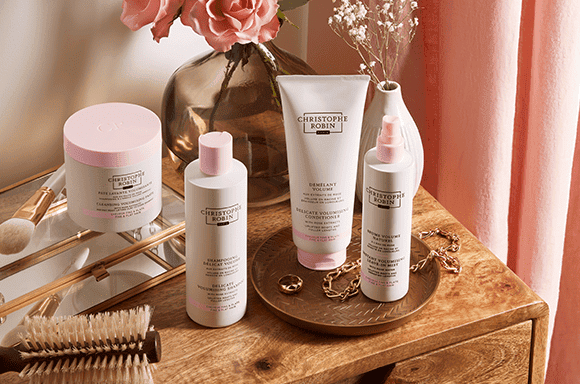 Four sustainable hair products by Christophe Robin's Volume range. Four white bottles with baby pink accents.