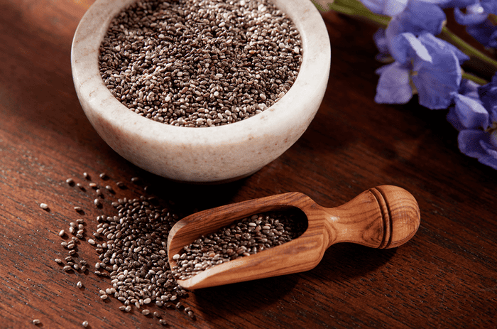 Chia seed oil for hair on a wooden table in a mortar bowl next to purple flowers.