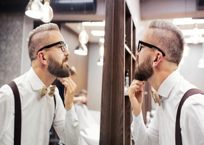 man with hipster beard looking in the mirror to check for beard growth