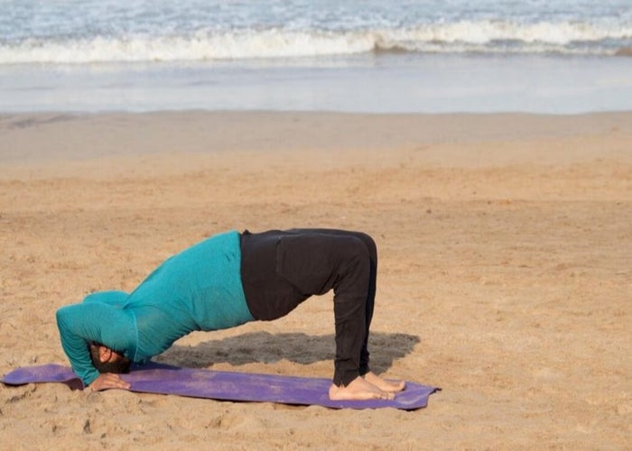 man in the half-bridge yoga pose at the beach