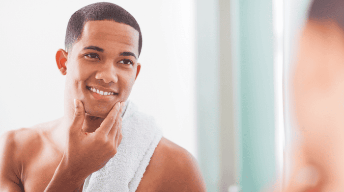 Young clean, shaved man touching the side of his face with a towel | Gillette UKg his face after shaving.