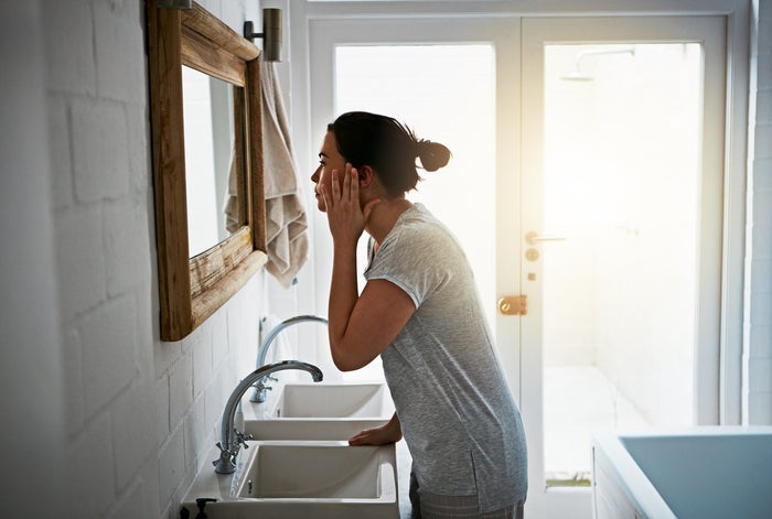 Woman stood over a sink looking at her reflection before dermaplaning | Venus UK