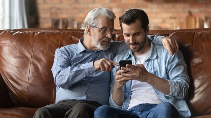 A well-groomed father and son play with a phone while sitting on a couch | Gillette UK