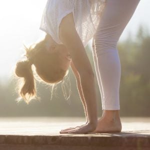 A woman stretching with her hands on the floor outside.