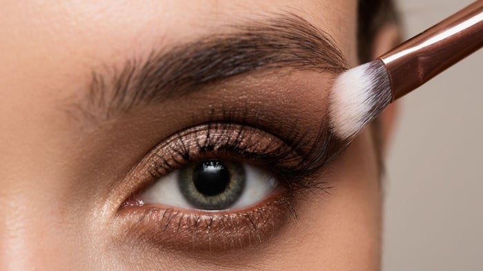 A close-up of one eye with natural holiday makeup being applied by an eyeshadow brush.