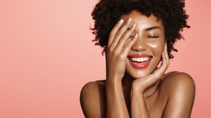 A young woman on a pink background glows thanks to soft glam.