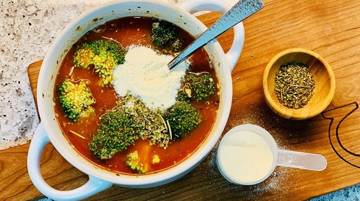 Birdseye view of tomato and broccoli soup, mixing in Klean Isolate powder.