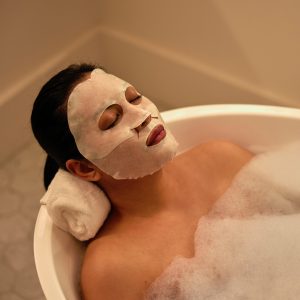 women laying in a bath tub relaxing with a sheet mask on
