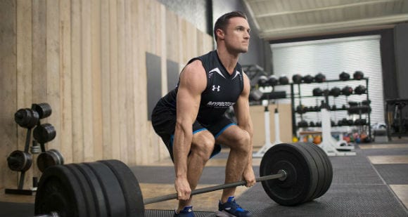 man in black gym tank and shorts performing a deadlift with barbell