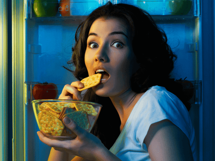 A woman sneaking crackers from the fridge