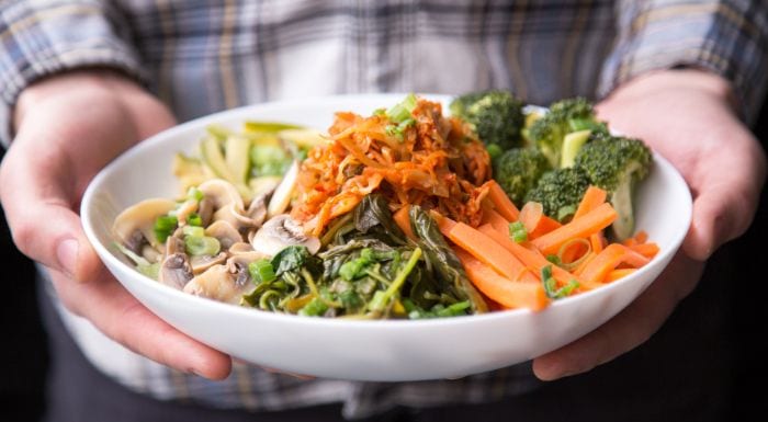 hands holding a bowl of cooked vegetables