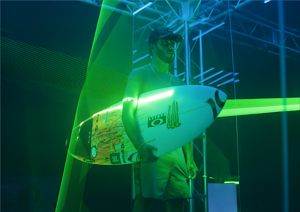 Man carrying a Monster Energy surfboard on a glowing green background