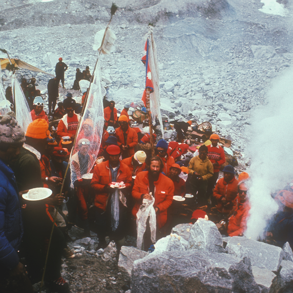 a group of people at a basecamp stood up eating all wearing red.