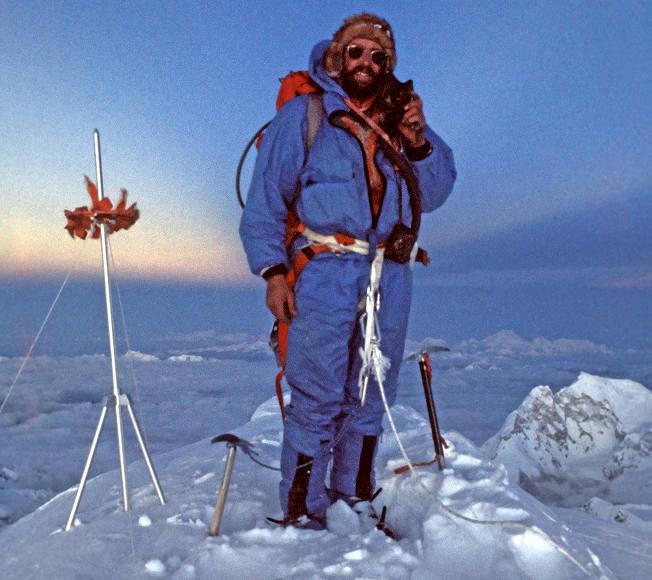 A man at the peak of a mountain smiling at the camera