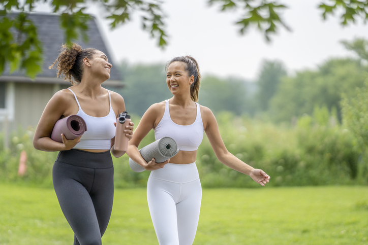 2 women outside holding a yoga mat