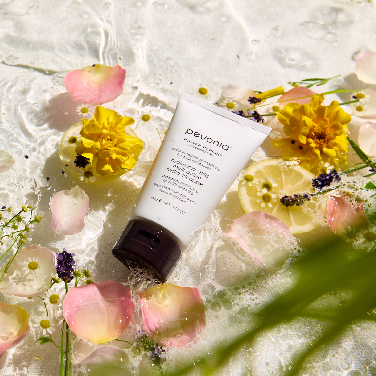 Pevonia's new Hyaluronic Acid cleanser lay in a bed of water, accompanied by the natural ingredients of the product including lemon, rose petals and Lavendar. 