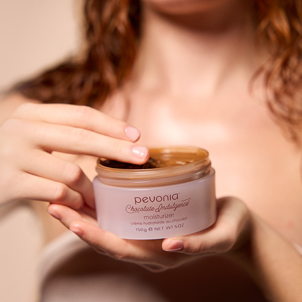 It is a Brown background  image with a model holding chocolate moisturizer.