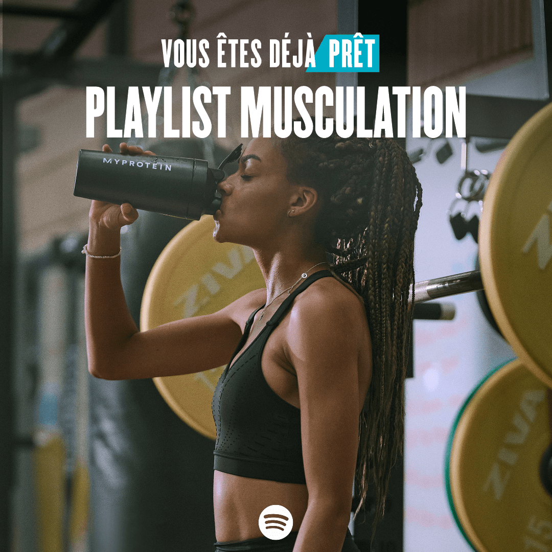 A woman wearing black workout clothes drinking from a black Myprotein shaker with the words 'You're Already Ready - Weightlifting Playlist' overlaying.