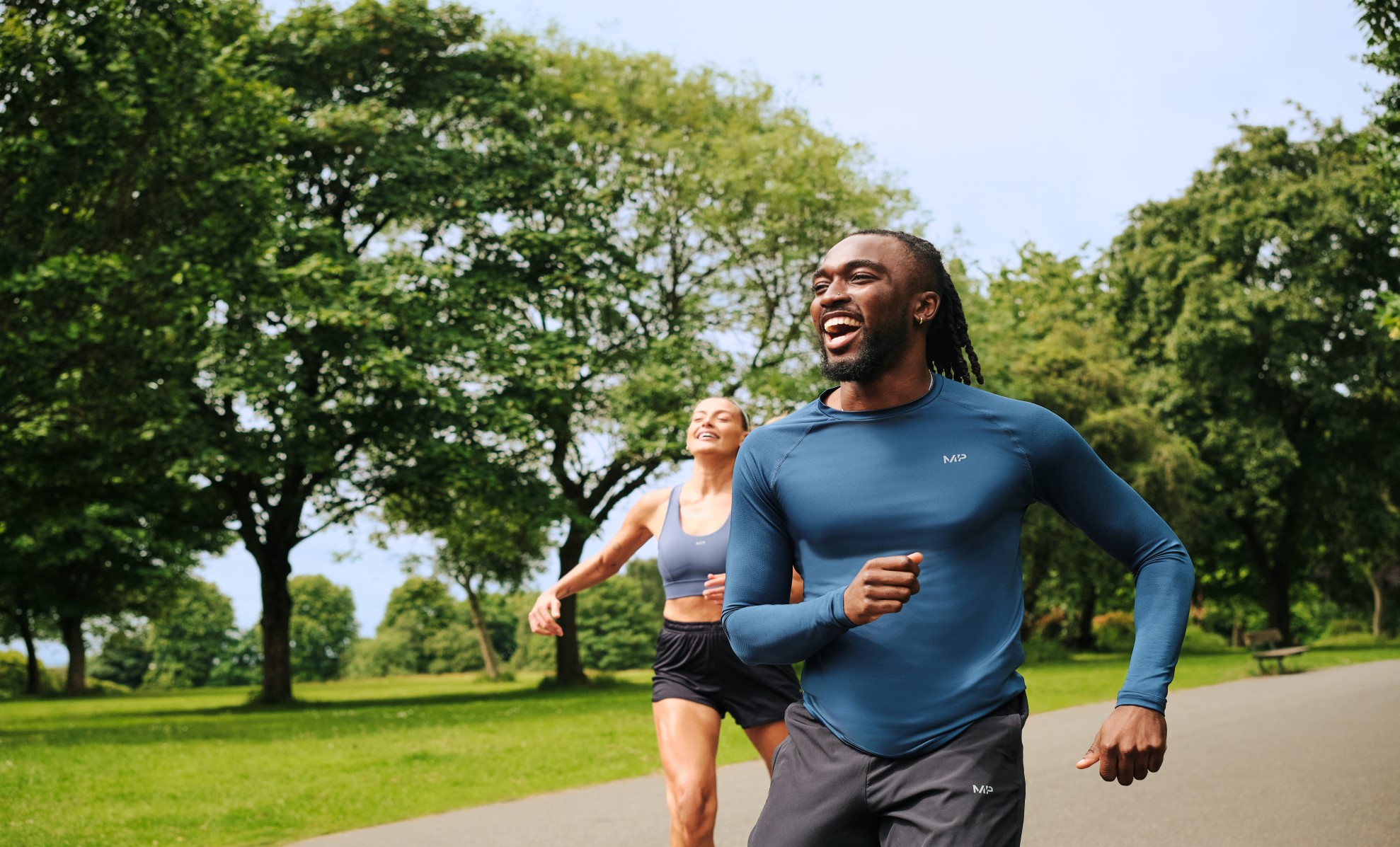 A man and a woman jogging in MP clothing through a public park smiling.