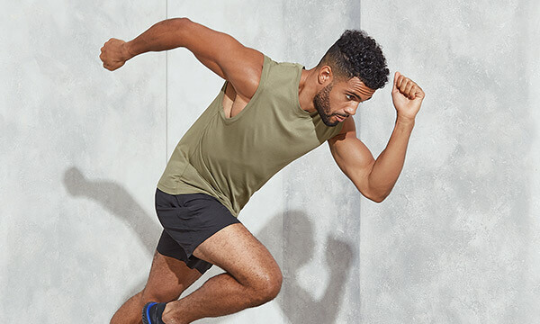 A man setting off running wearing a army green tank top and black gym shorts.